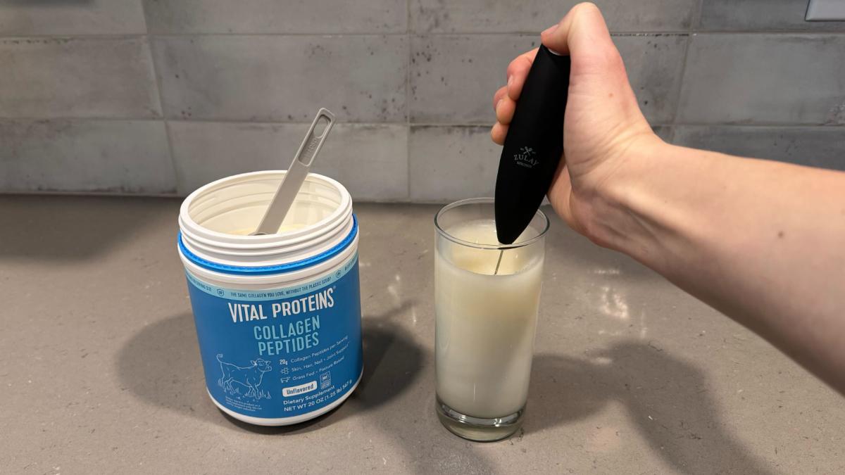 A person using an electric frother to mix unflavored Vital Proteins Collagen Peptides with water in a clear glass